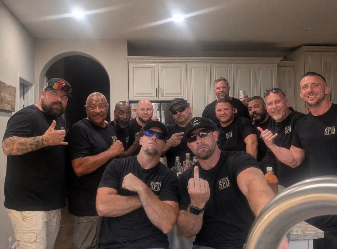 Whole crew packed in the kitchen — peace signs and middle fingers up