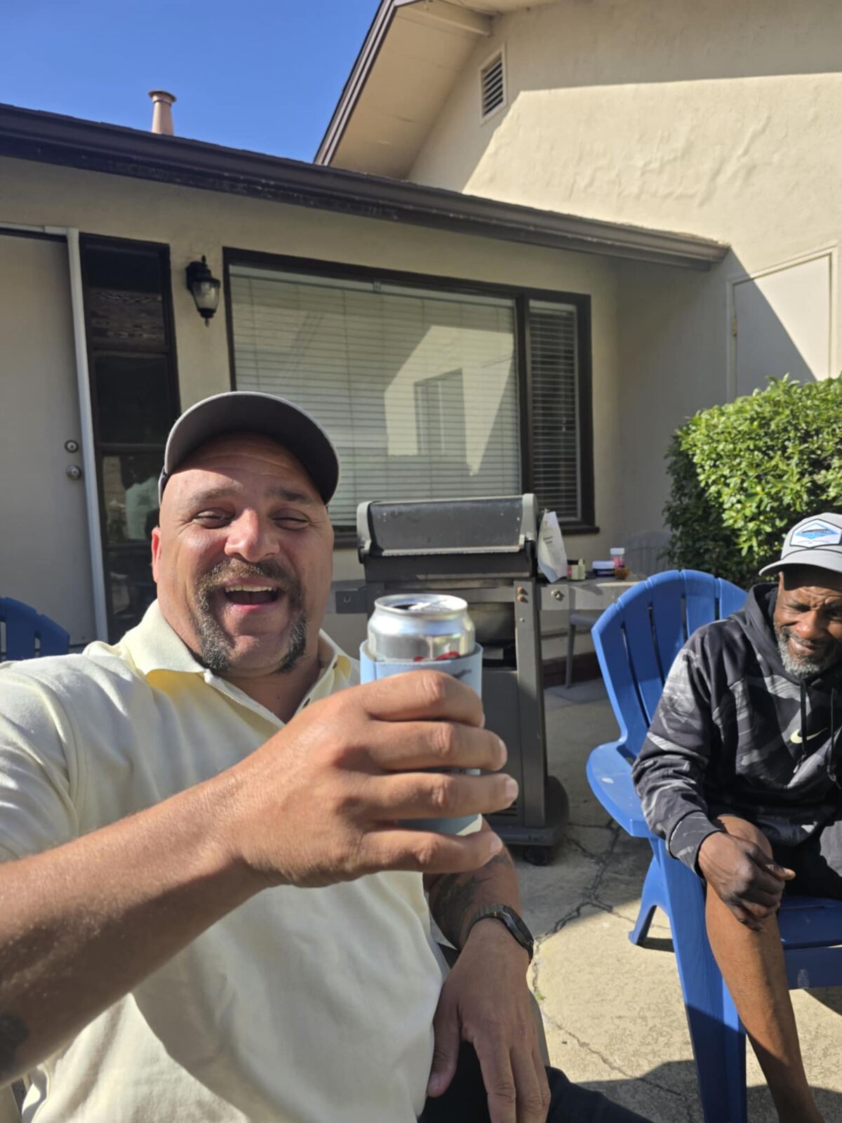 Backyard cheers — koozie up, blue chairs, neighborhood sun