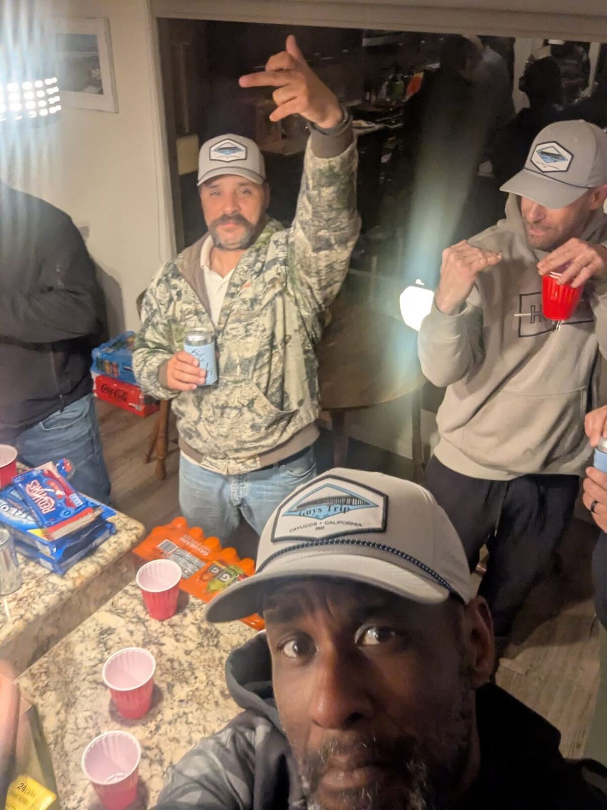 Cayucos selfie — matching Guys Trip caps and red cups in hand