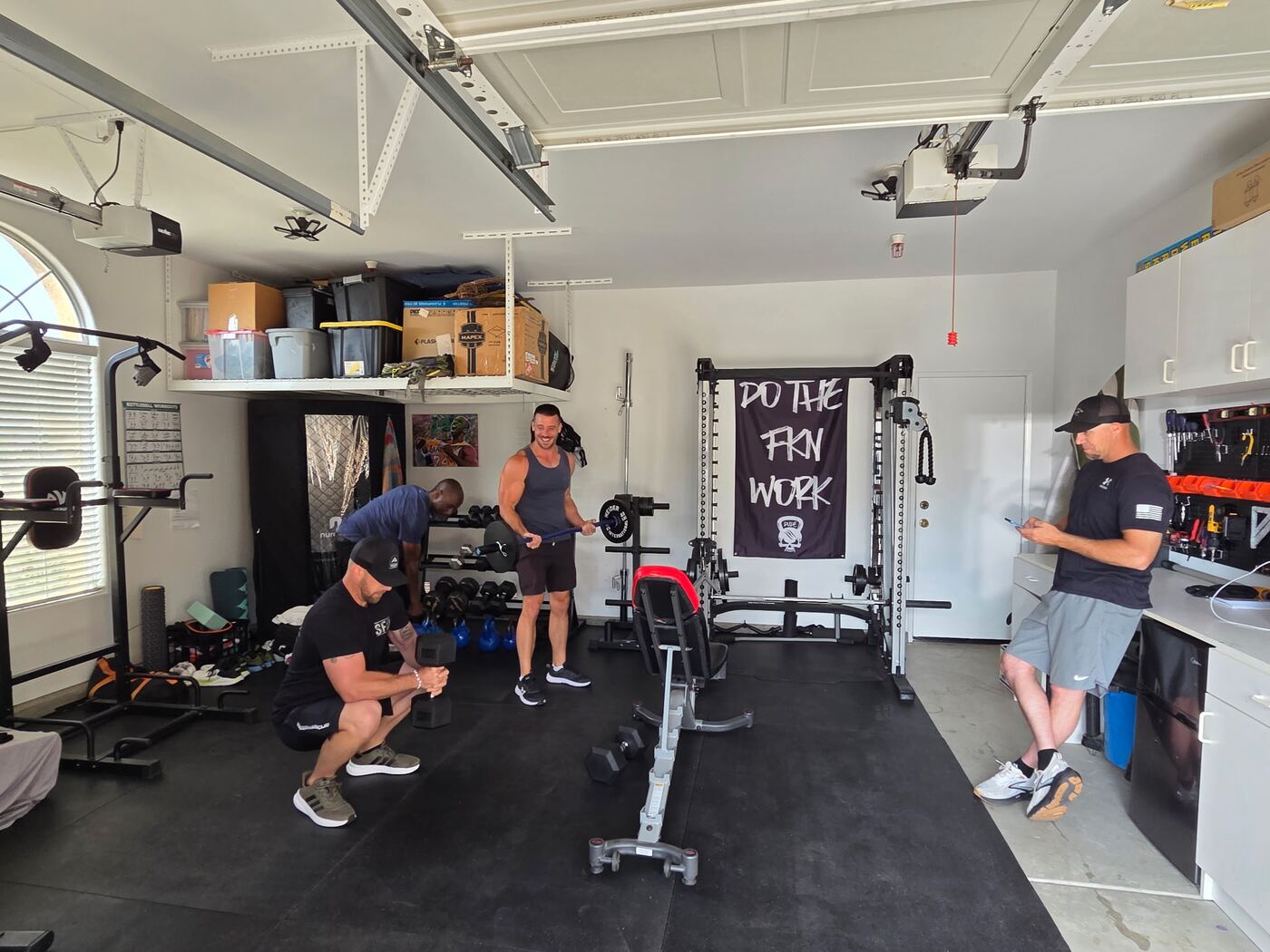 Garage gym session under the 'Do The F*ckn Work' flag — squats and barbell