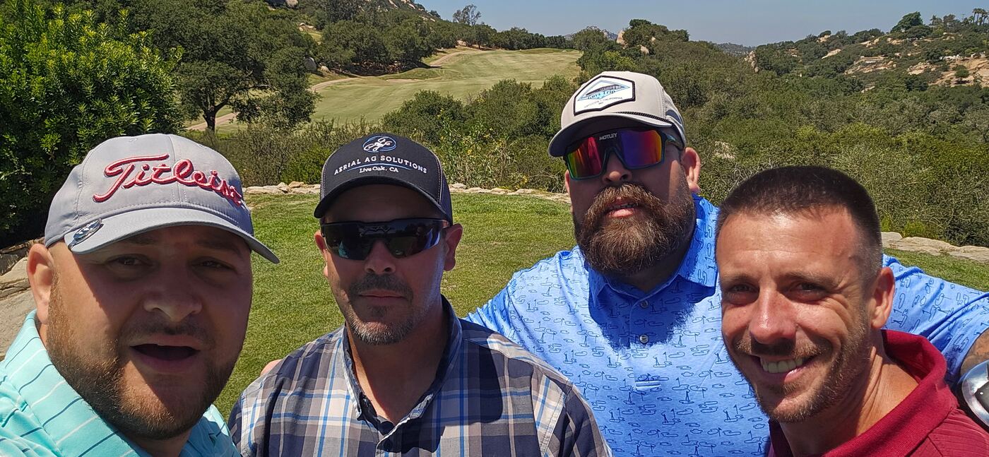 Foursome selfie at the overlook — fairway dropping off behind us