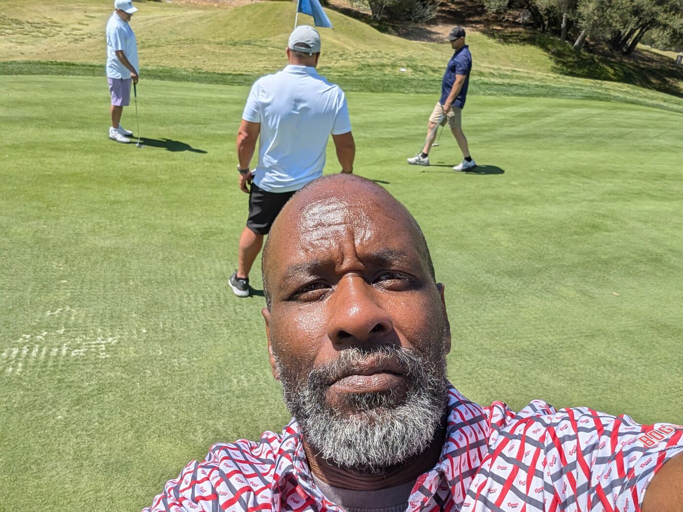 Selfie on the green — three brothers lining up putts in the background
