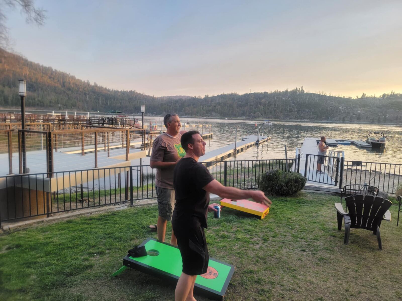 Cornhole at golden hour — boards on the lawn, lake glassing off