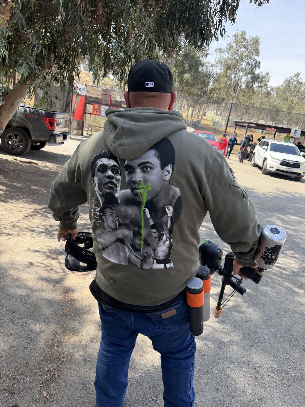 Ali hoodie from the back — marker holstered, can in hand, walking the lot