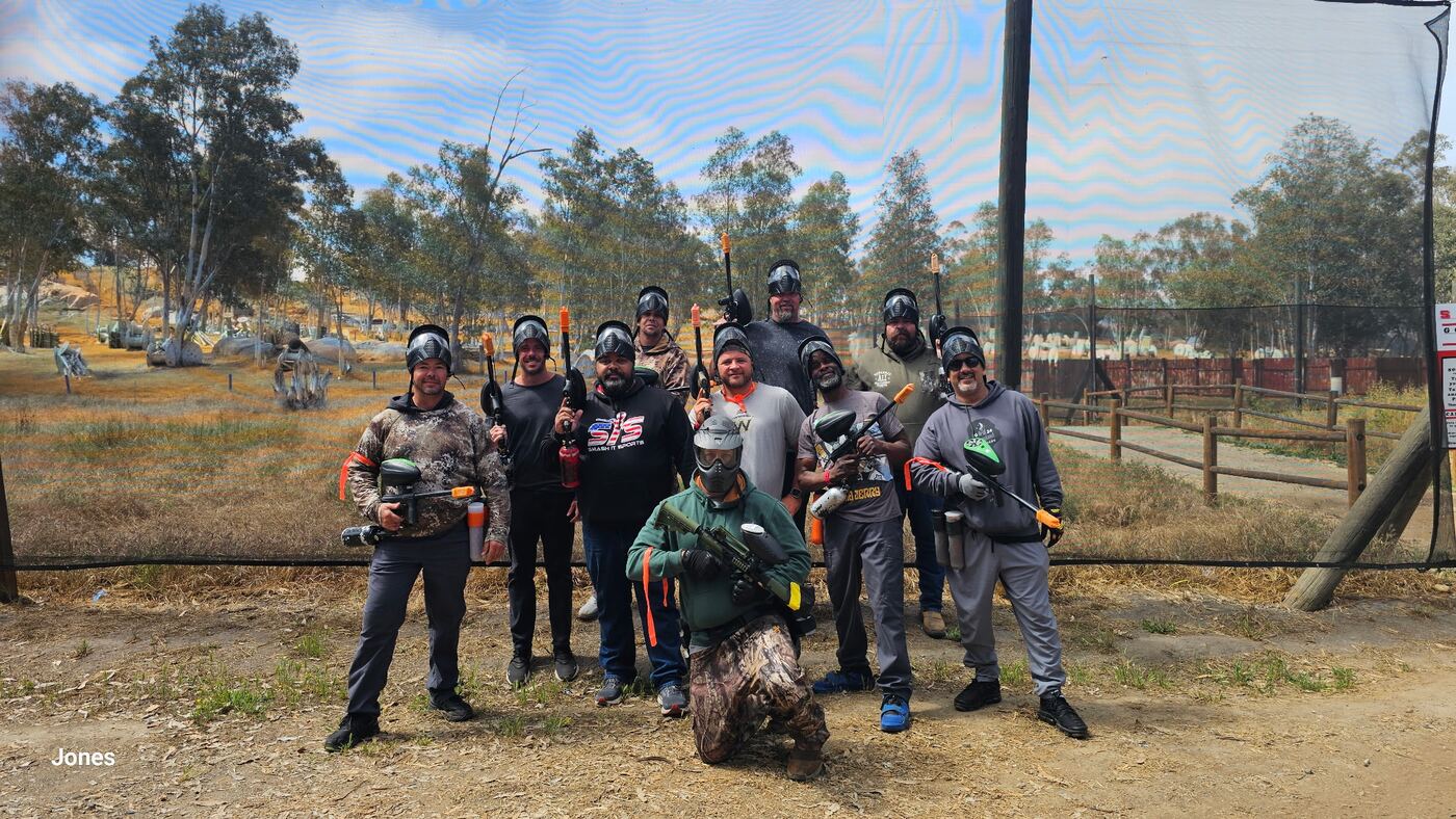 Whole paintball crew lined up at the field — masks up, markers ready