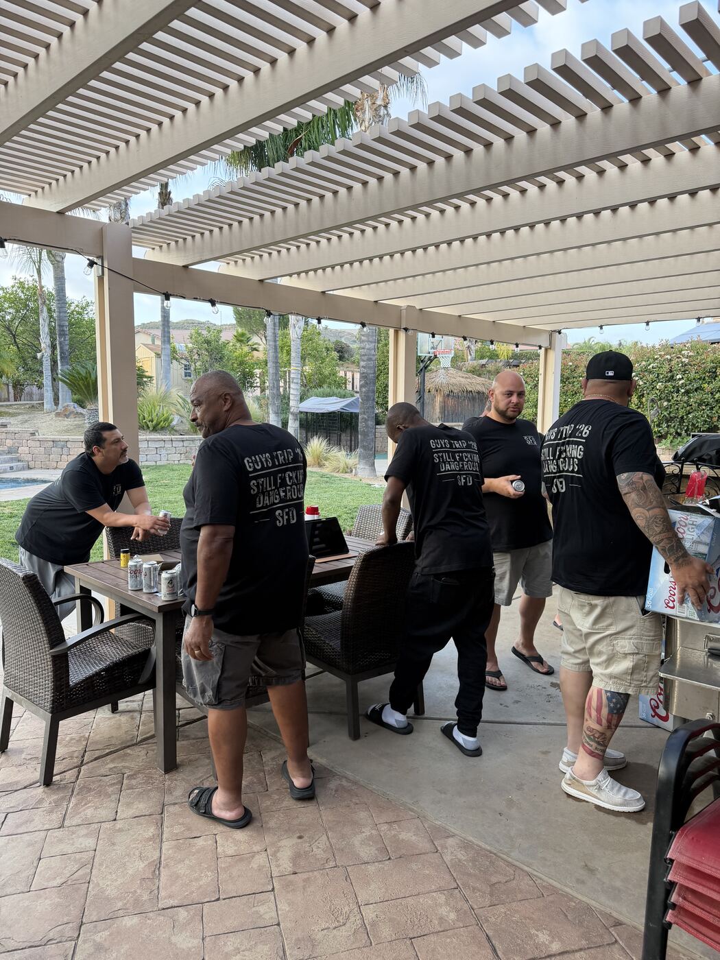 Crew under the pergola in 'Still F’cking Dangerous' tees — beers down, Coors on deck