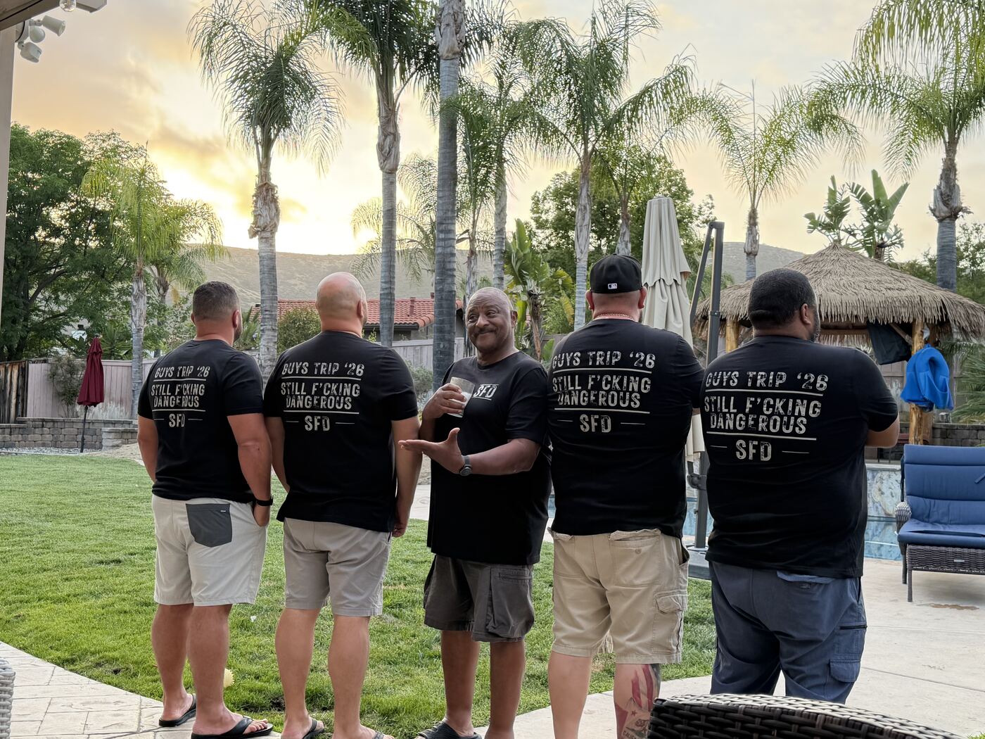 Five brothers in matching Guys Trip '26 tees — palm-tree sunset over the backyard